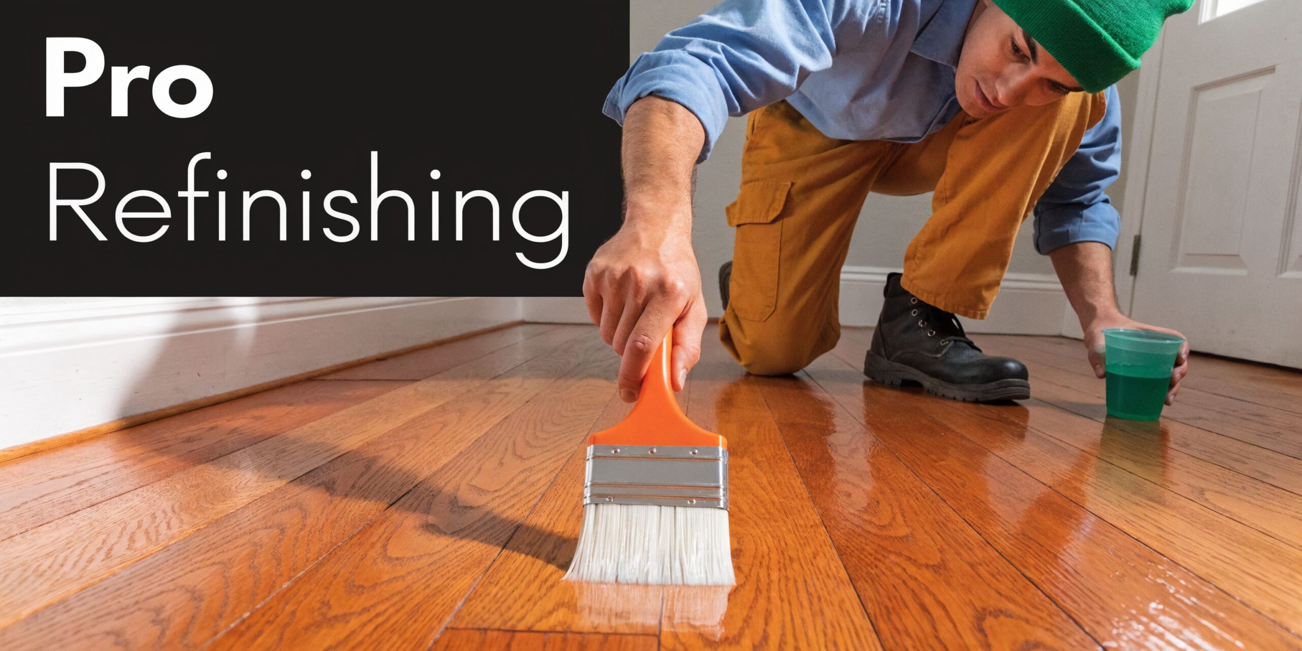 A professional tradesman in a green beanie refinishing a beautiful, shiny hardwood floor with a brush.