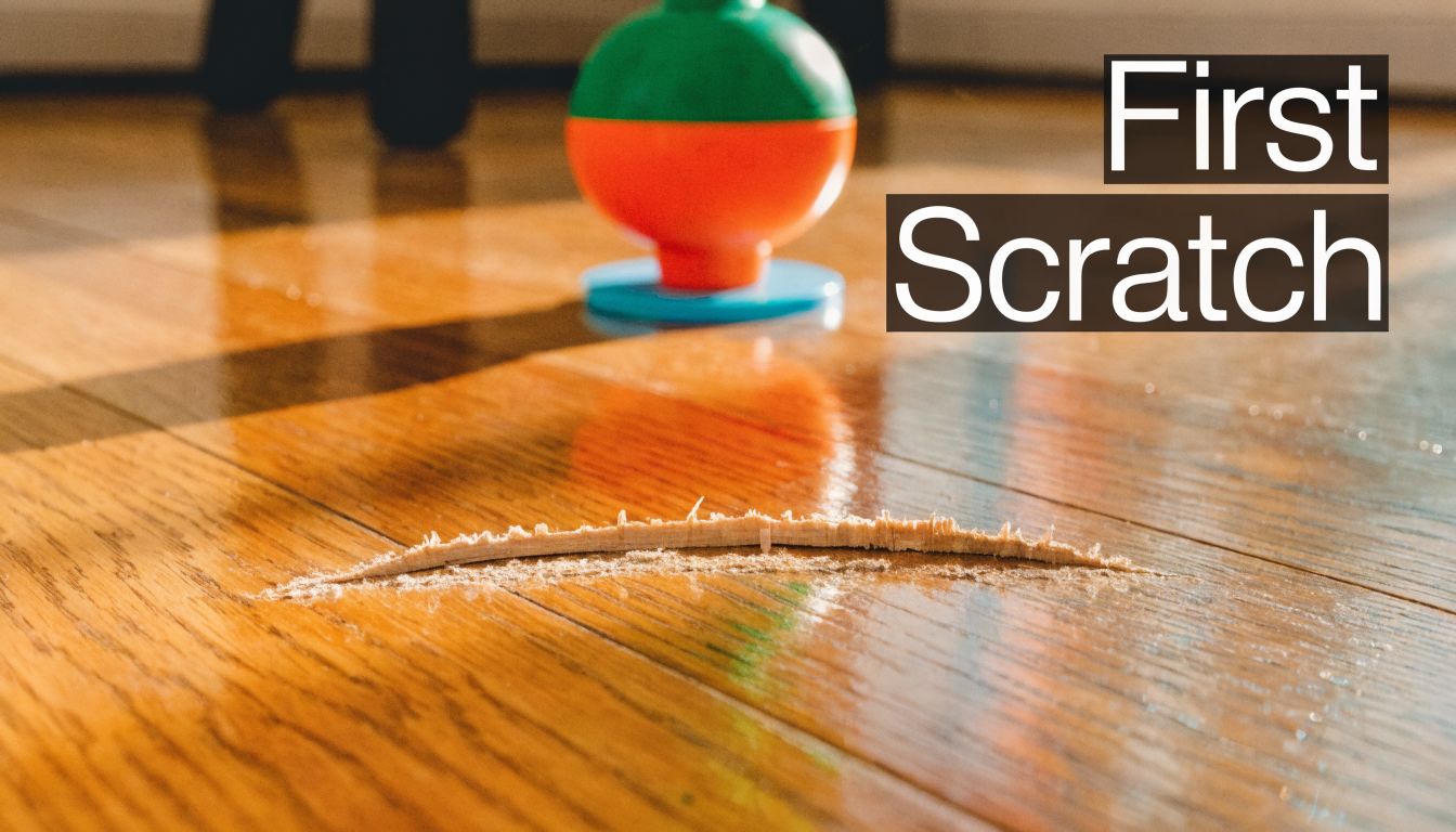 A deep scratch on a polished hardwood floor near a colorful child's toy on the floor.